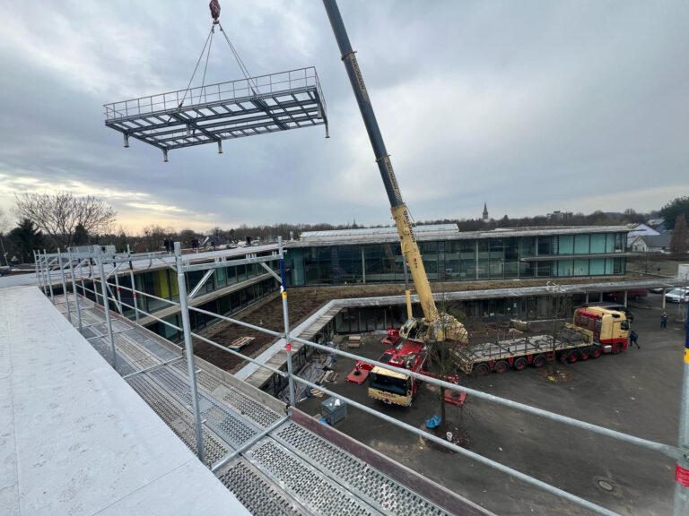 Montage eines verzinkten Stahlrahmens mit Kran auf dem Dach eines Schulgebäudes in Leverkusen – präzise Positionierung durch BEWA Industrieservice.